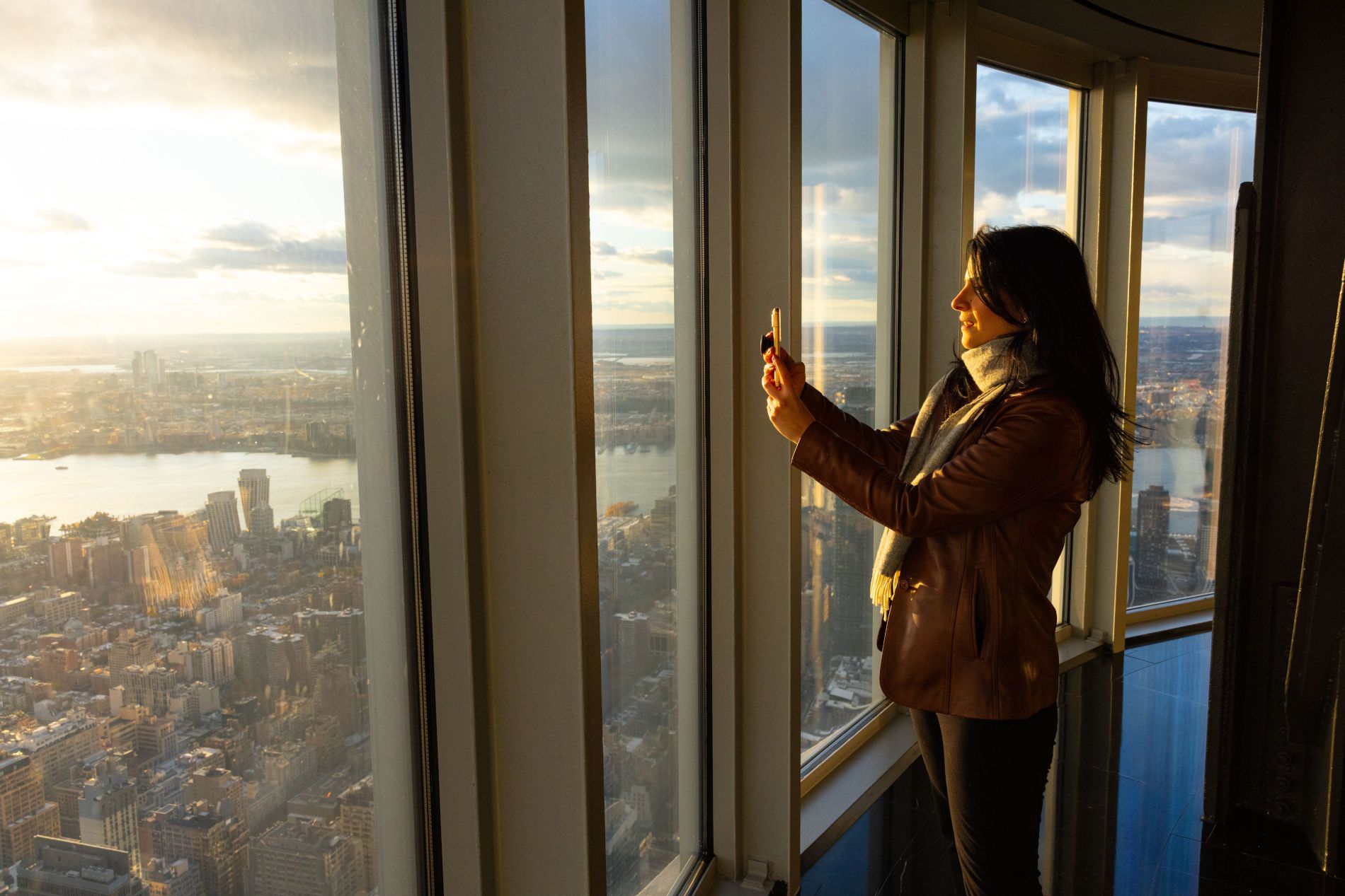 Giovane donna che scatta una foto del tramonto dal 102º piano dell'Empire State Building a New York